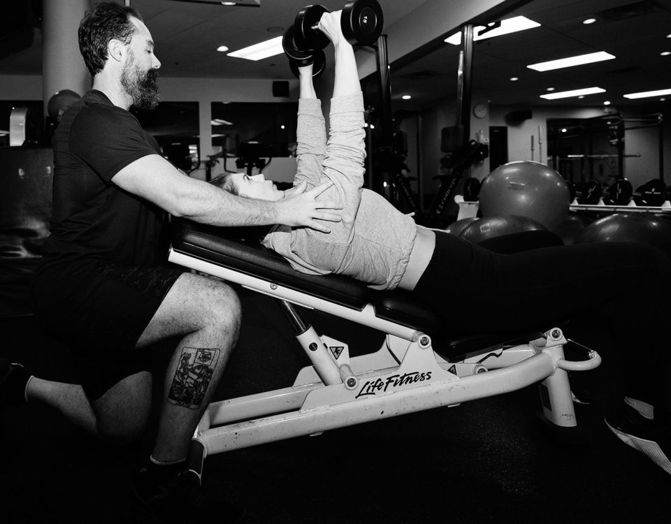 TurnFit coach spotting a midlife woman on an incline press — the opposite of uncoached home workouts