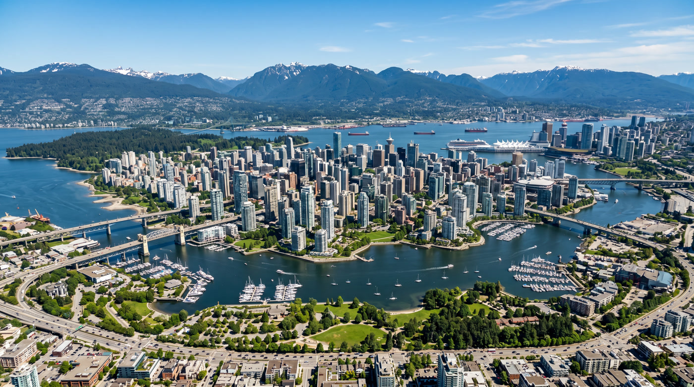 Aerial view of Vancouver BC business district — downtown skyline, False Creek, Stanley Park, Burrard Inlet, and North Shore mountains on a clear sunny day